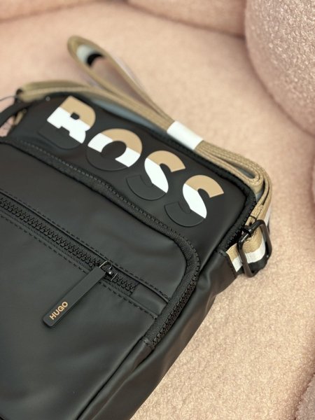 الحقيبة الظاهرة في الصورة هي حقيبة كتف سوداء من ماركة هوغو بوس (Hugo Boss).